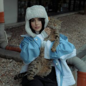 Stylish woman in a blue jacket and hat holding a tabby cat outdoors.